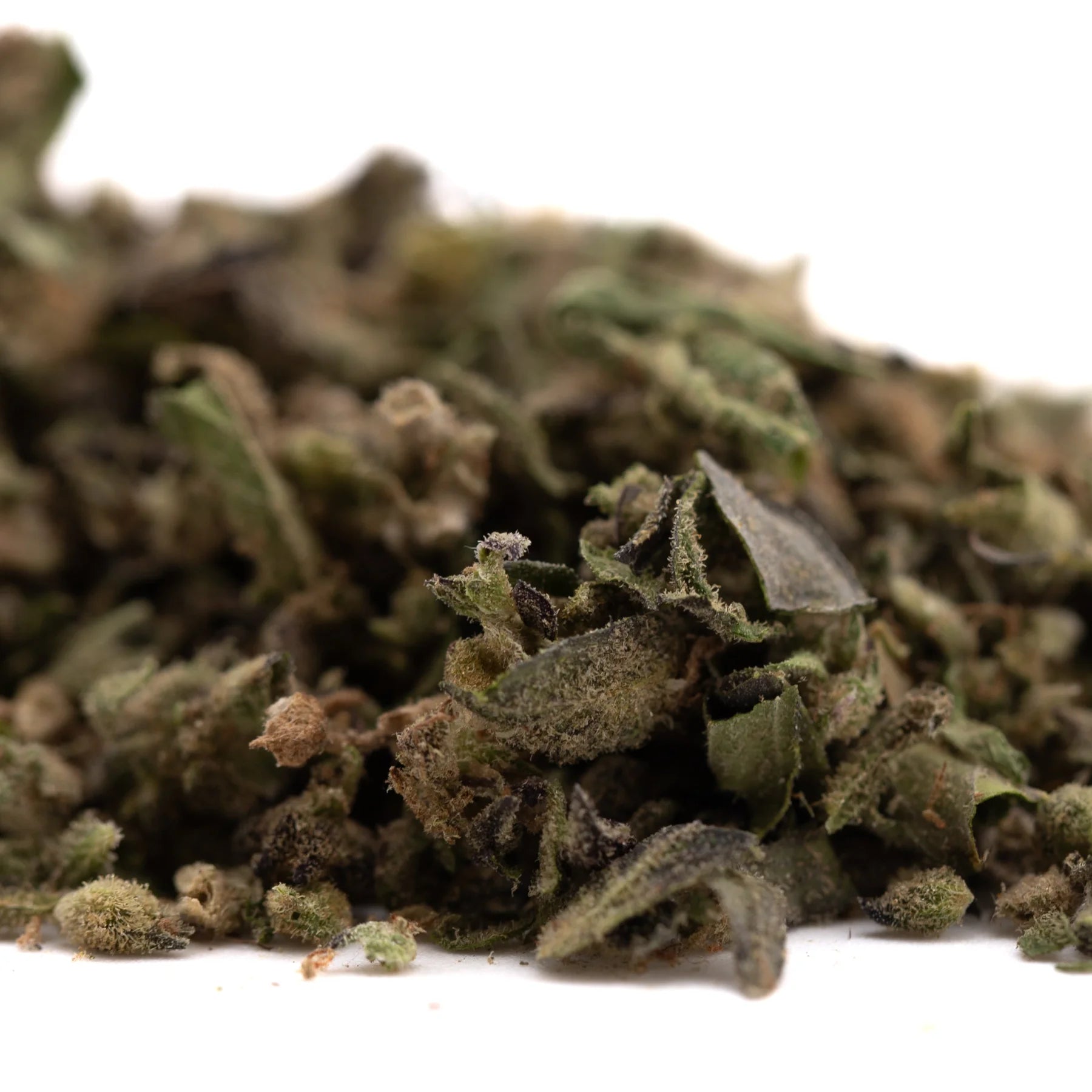 A pile of dried cream caramel full-term thca trim hemp flower leaves with visible trichomes in green and brown hues