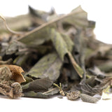 A pile of dried muted green and brown greenhouse thca trim wholesale with fuzzy stems kush phenotype leaves