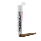 White cylindrical container labeled gas monkey thc-a premium pre-roll next to an unrolled brown paper joint for thca pre-rolls