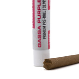 A white cylindrical tube labeled gassa purple premium pre-roll in red text with a brown paper thca blunt beside it