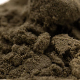A mound of coarse dark brown thca kief with a rough texture from garlic cookies cult top-shelf indoor product