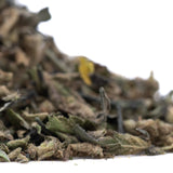 A pile of dried green and brown full-term thca flower trim with a yellow petal showcasing indoor cultivation terpene profile