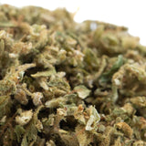 A dense tune cbd hemp flower trim bud with green and amber hues covered in white trichomes pre-converted cbd