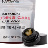 Black glass jar of golden-yellow wedding cake thca dab wax 1g with open lid beside it for concentrate use