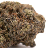 A dense, textured black amber indoor thca flower bud covered in green and brown trichomes with an irregular shape