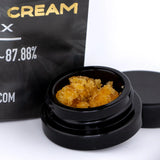 Black glass jar containing golden-orange cookies and cream 91.52% cbd dab wax for dabbing use