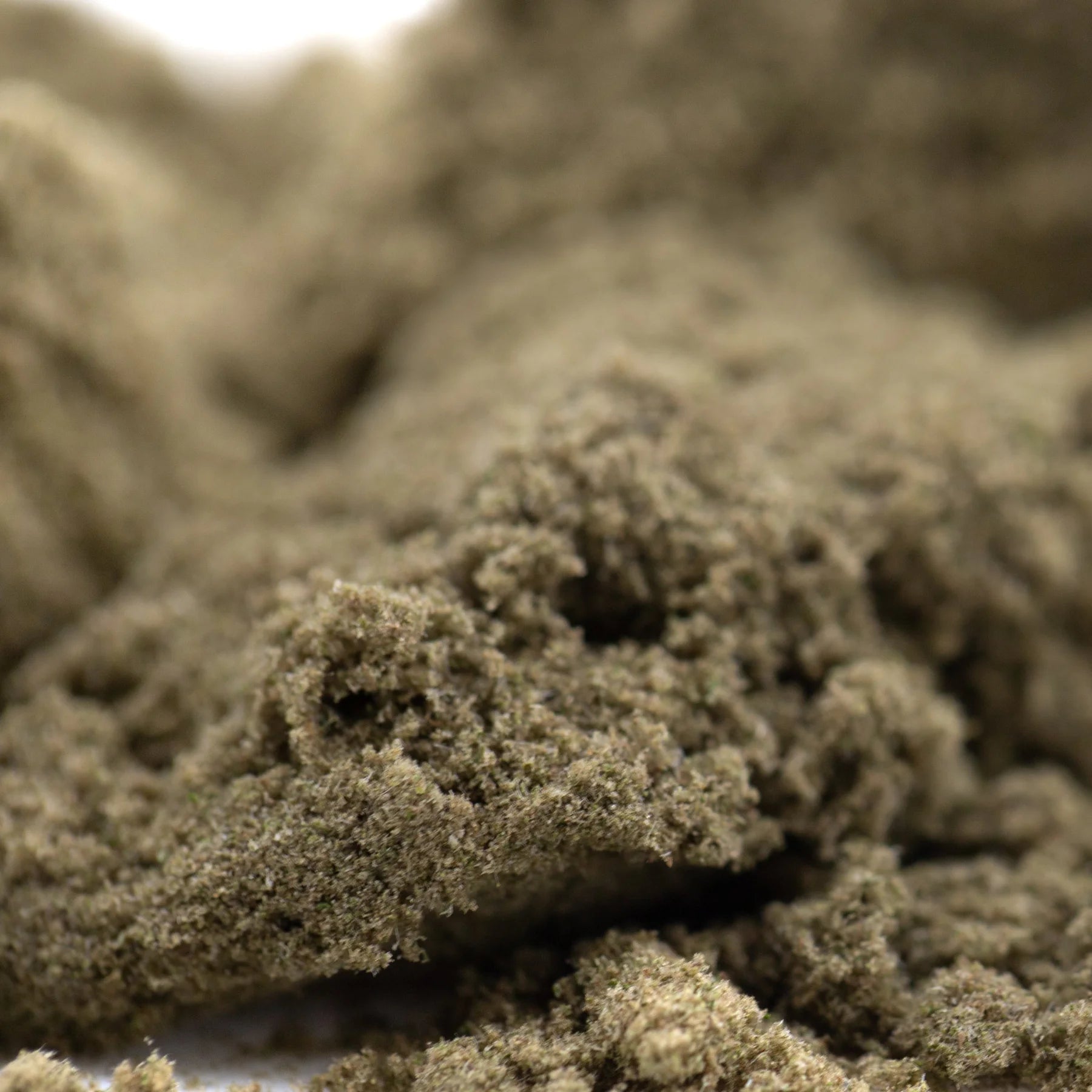 A mound of coarse beige cream caramel thca kief showcasing textured hemp flower product material