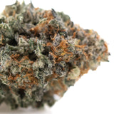 A dense frosty kali snapple indoor thca flower bud with green and orange hues and tropical pineapple aroma