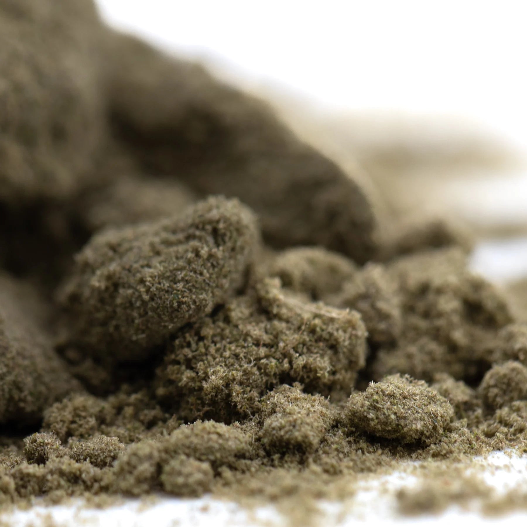 A pile of coarse earthy-brown mendo breath thca kief with a textured fibrous surface cult classic cannabis flower