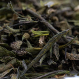 A pile of premium greenhouse purple marmalade thca trim with dried green tea leaves showing terpene profile effects
