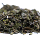 A pile of dried green tea leaves with delicate stems and curled edges in premium greenhouse purple marmalade thca trim