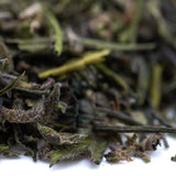A pile of dried green tea leaves with curled edges in premium greenhouse purple marmalade thca trim with terpene profile