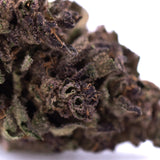 Dense dark purple cannabis bud with trichomes and green leaves from purple queens greenhouse thca flower total cannabinoid