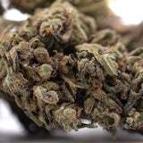 A dense resinous rna full-term cbd hemp flower bud with green and brown hues covered in fine trichomes and elevated cbg