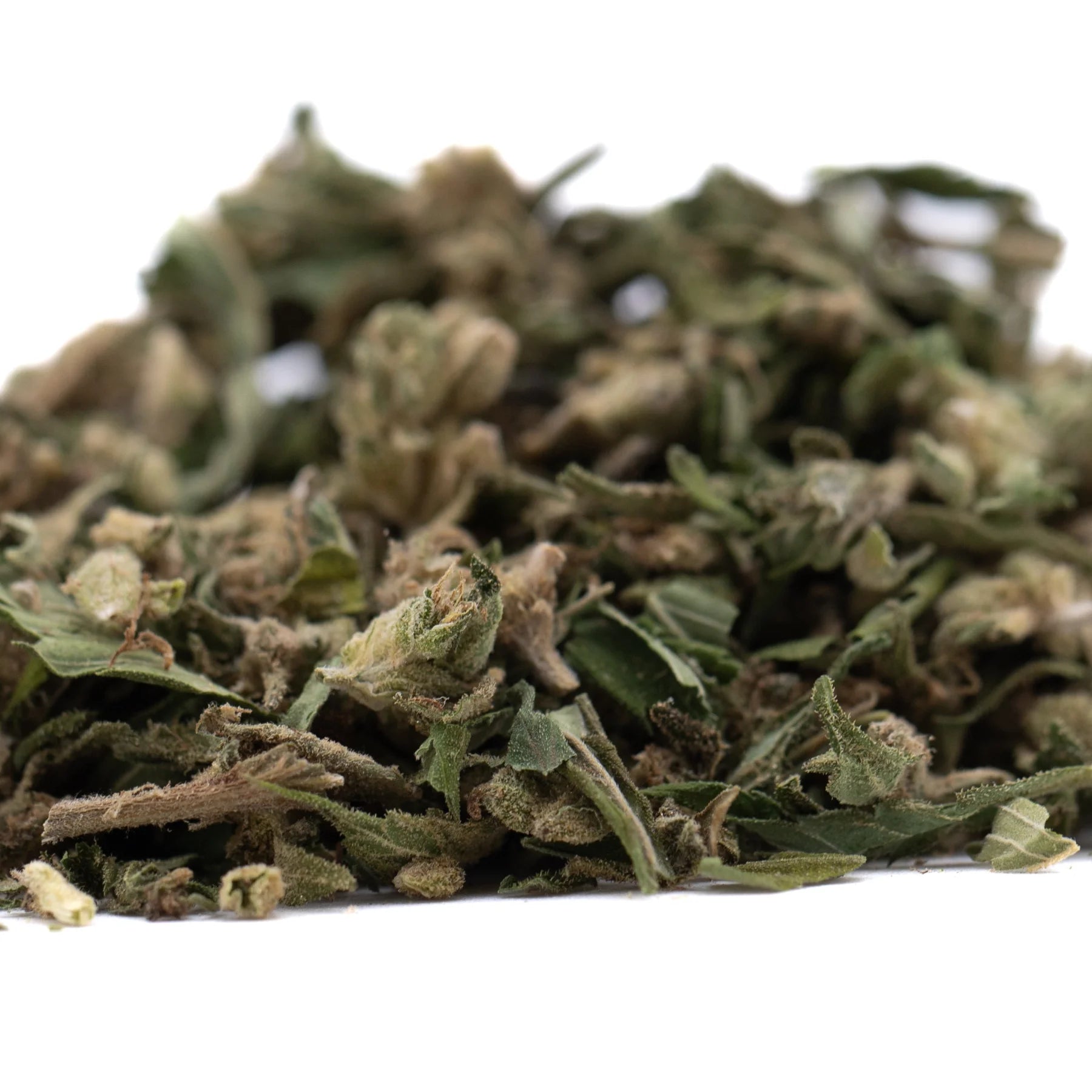 A pile of dried greenish-brown full-term thca flower trim with stems and leaves highlighting its terpene profile from indoor cultivation