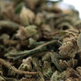A close-up of sour diesel full-term thca trim wholesale hemp flower with green and brown hues covered in fine trichomes