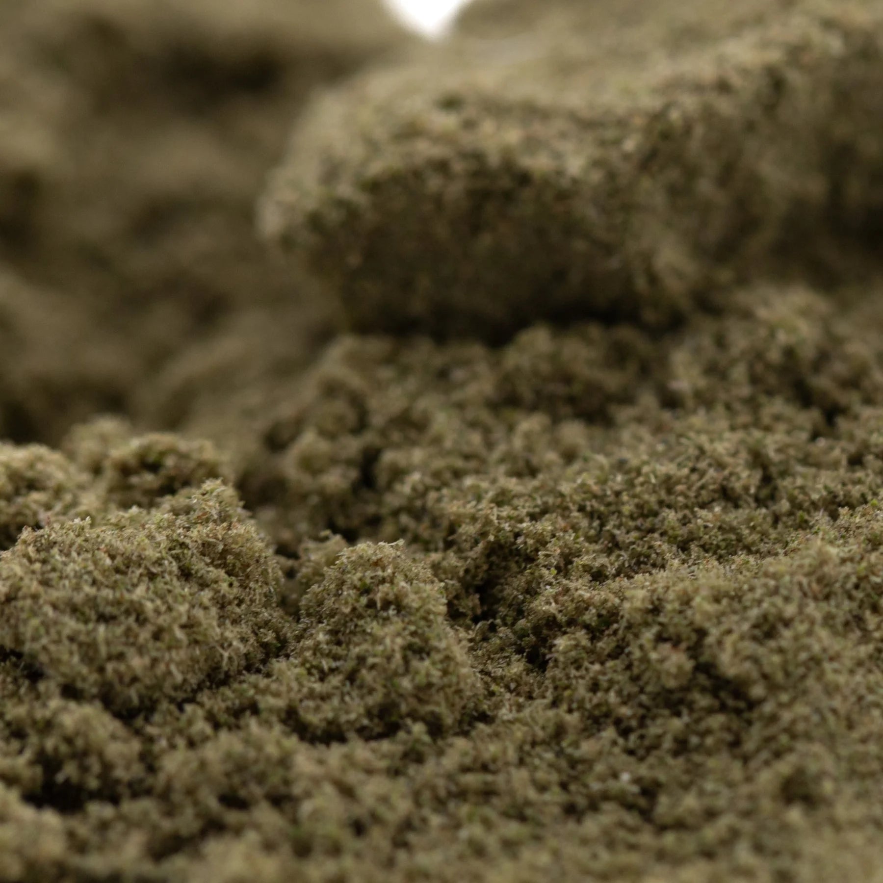 A close-up of coarse greenish-brown sour diesel thca kief with gritty texture for legendary fuel mexican sativa use