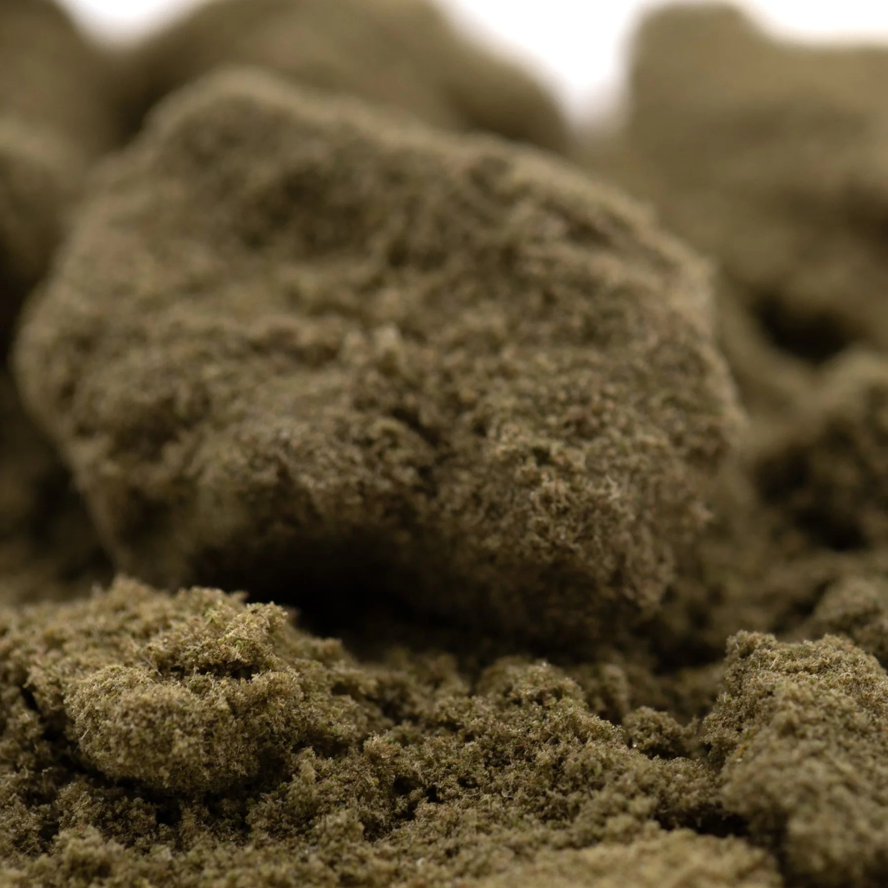 A textured earthy greenish-brown kief full-term cannabis concentrate with a dense crumbly consistency and dessert flavor strawberry cheesecake thca