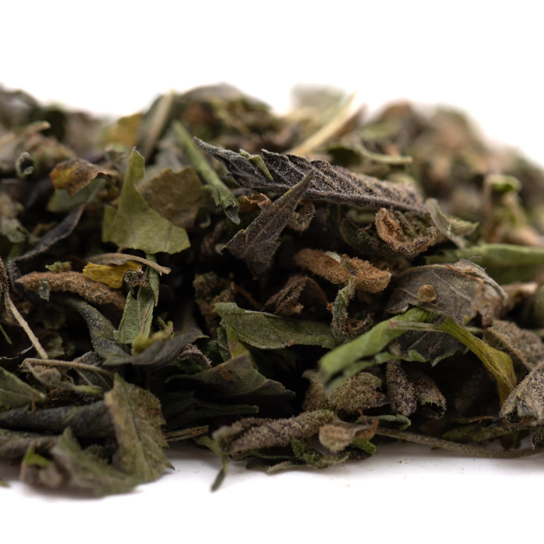 A pile of dried dark green and brown thca shake herbal leaves with stems from greenhouse zushi kush mints flower trim